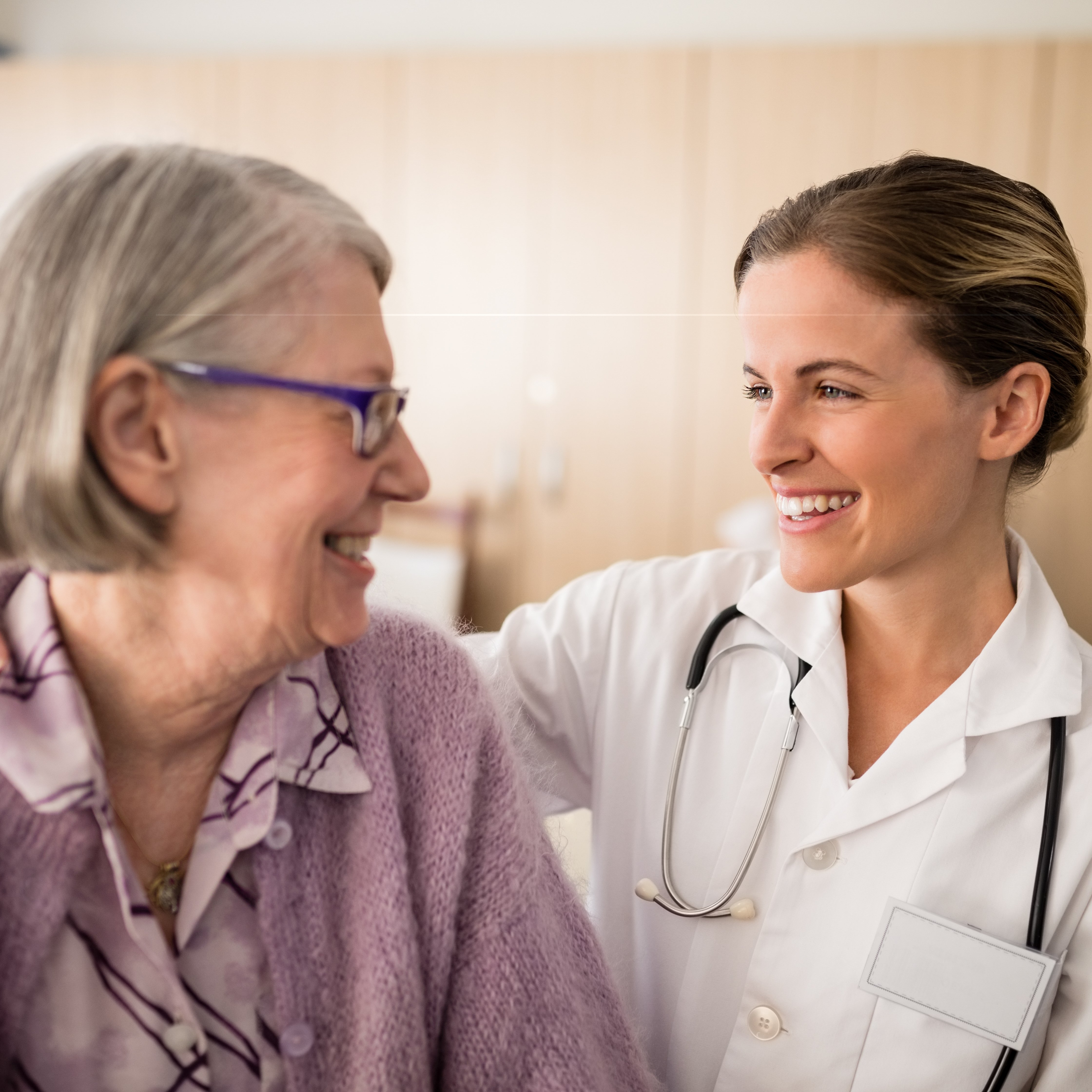 Smiling female doctor looking at senior woman with arm around in retirement home